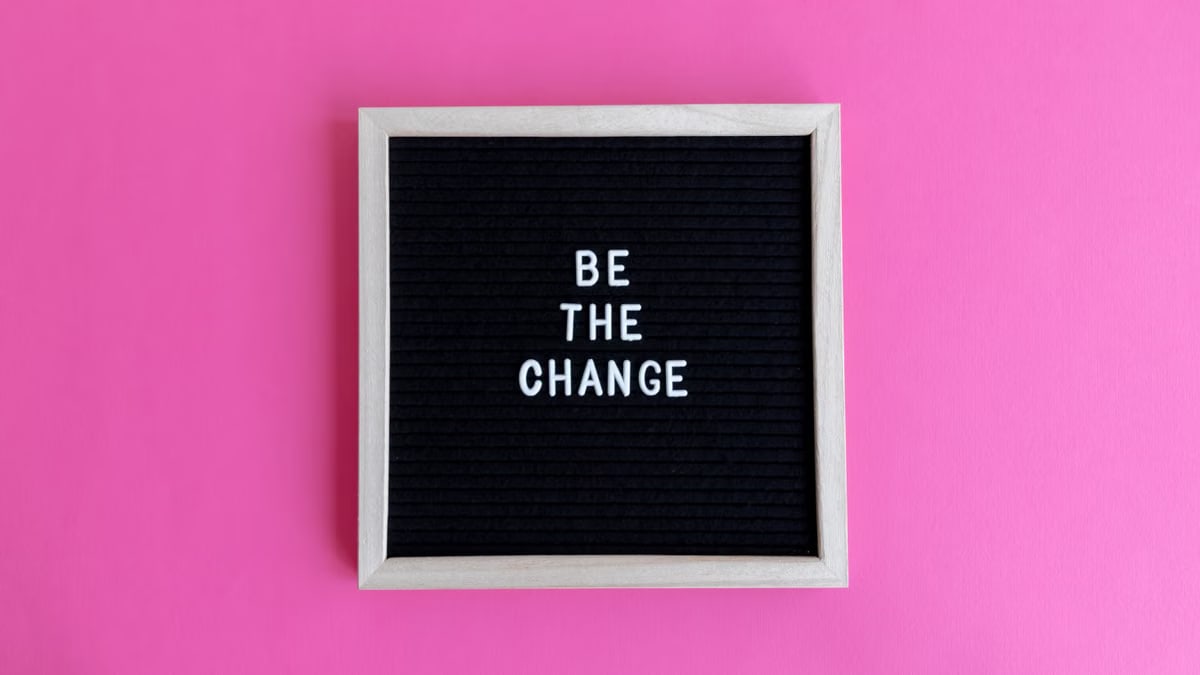 Letterboard with 'Be the Change' on a vibrant pink background.